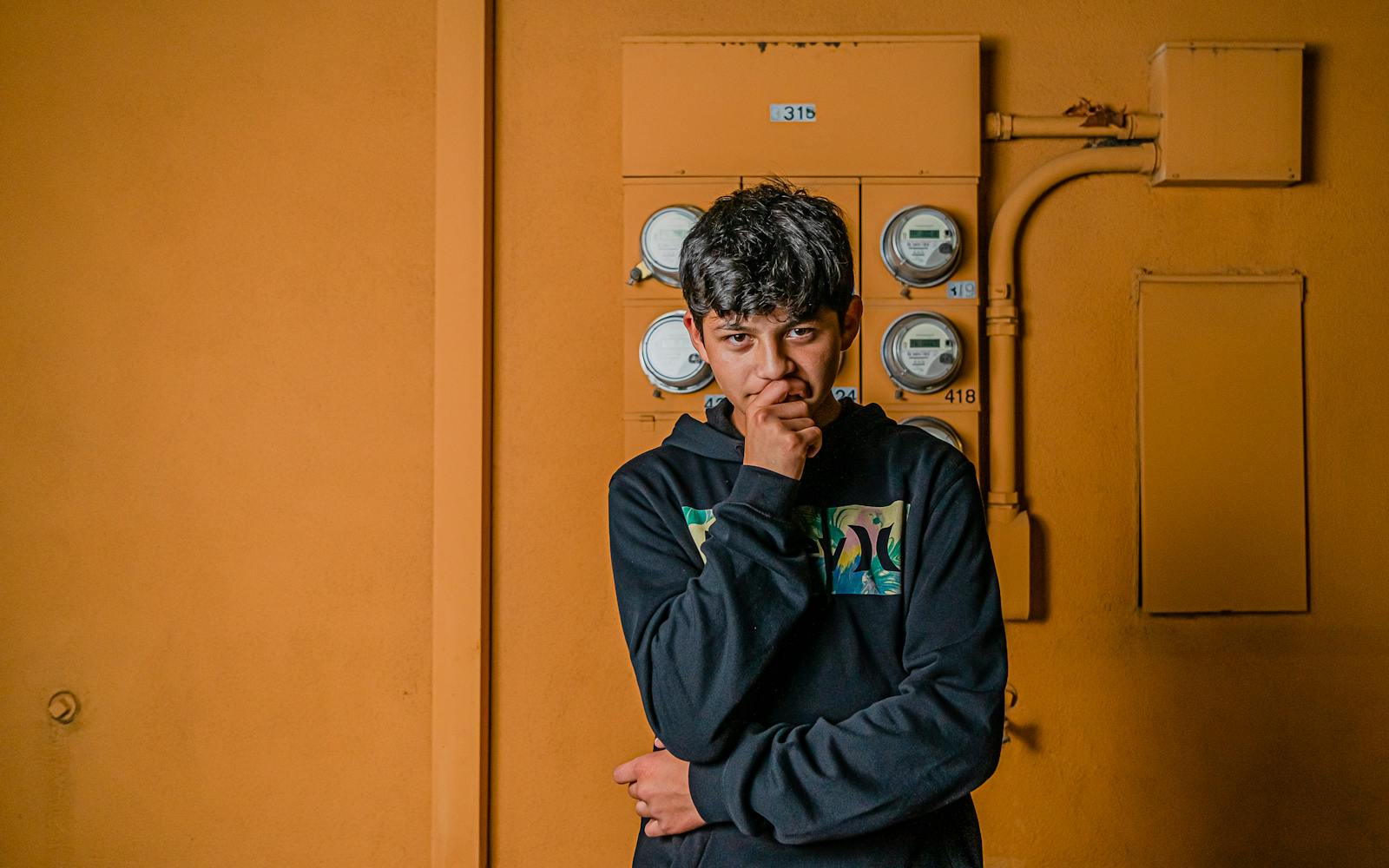 A young man thoughtfully poses in front of a yellow wall in Fullerton, CA.